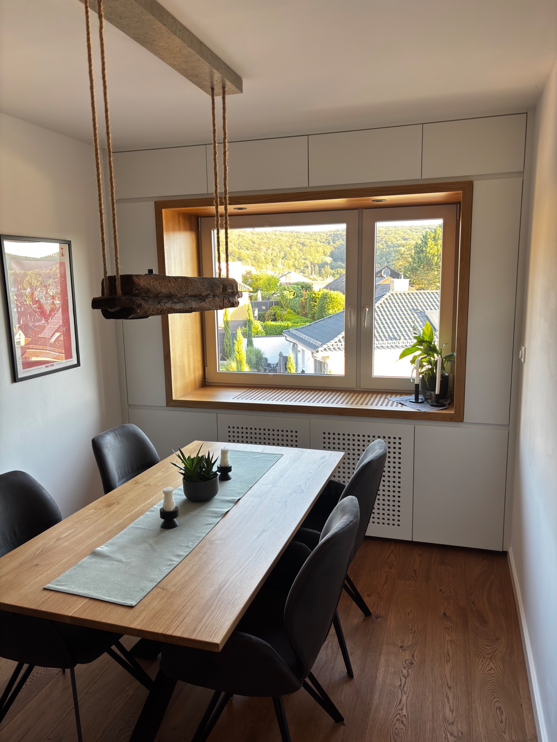 Sitzfensterbank in Einbauschrankwand, mit integrierter Heizkörperverkleidung. Esstisch und abgehängte Deckenlampe